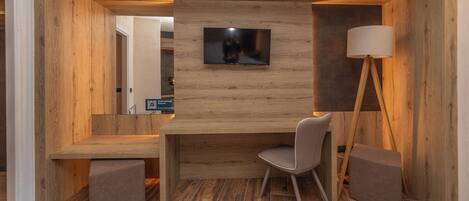 A modern, compact room with a wooden desk, a television mounted on the wall, and a floor lamp.