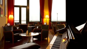 Una habitación de hotel con un piano de cola, asientos cómodos y ventanas grandes con cortinas.