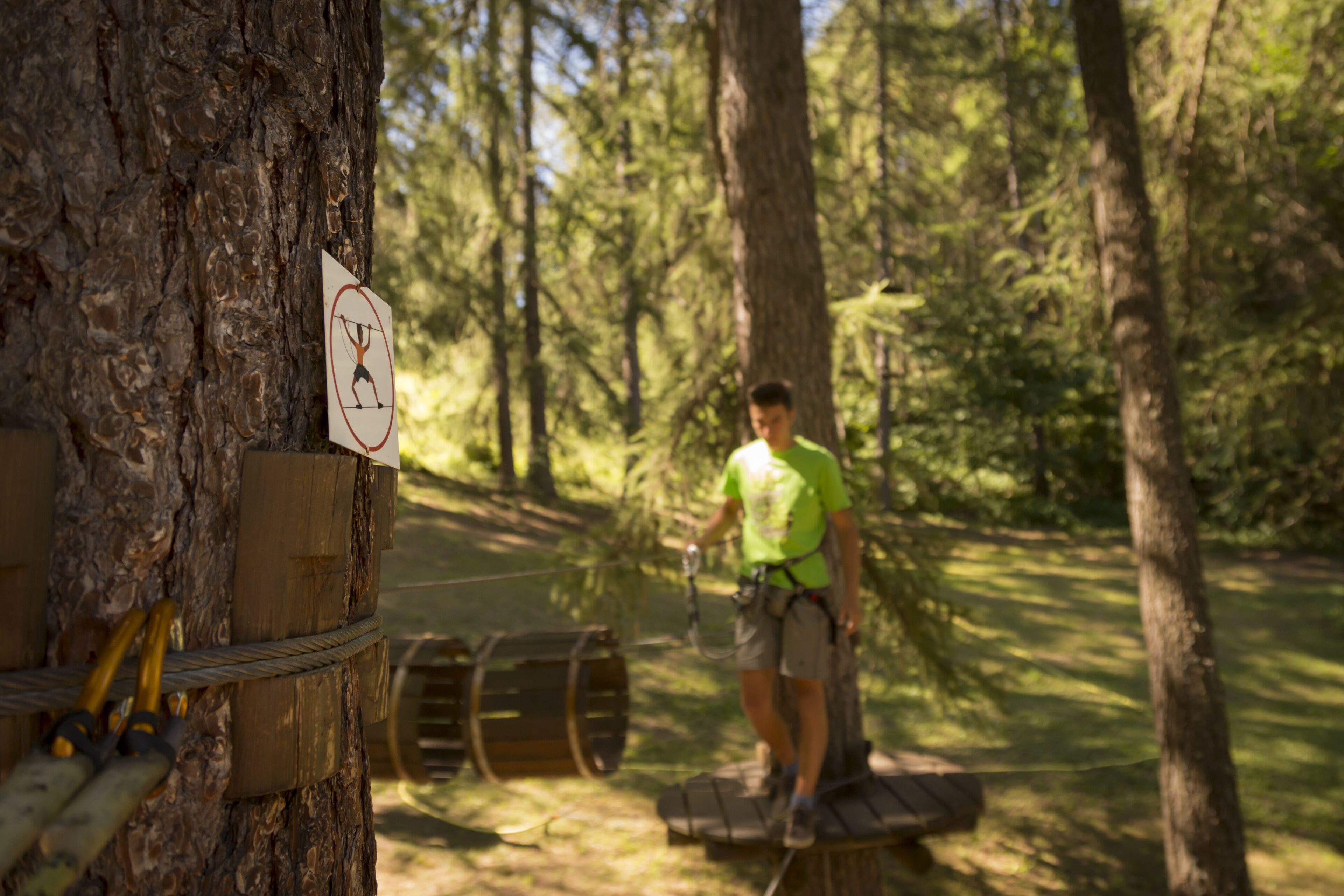 A person on a zip line in a wooded area with a sign on a tree indicating no climbing.