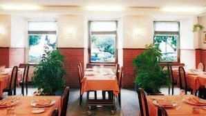 Un restaurant avec des tables dressées pour le service, de grandes fenêtres offrant une vue agréable et des plantes en pot.