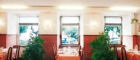 A restaurant with tables set for dining, large windows with views, and potted plants.
