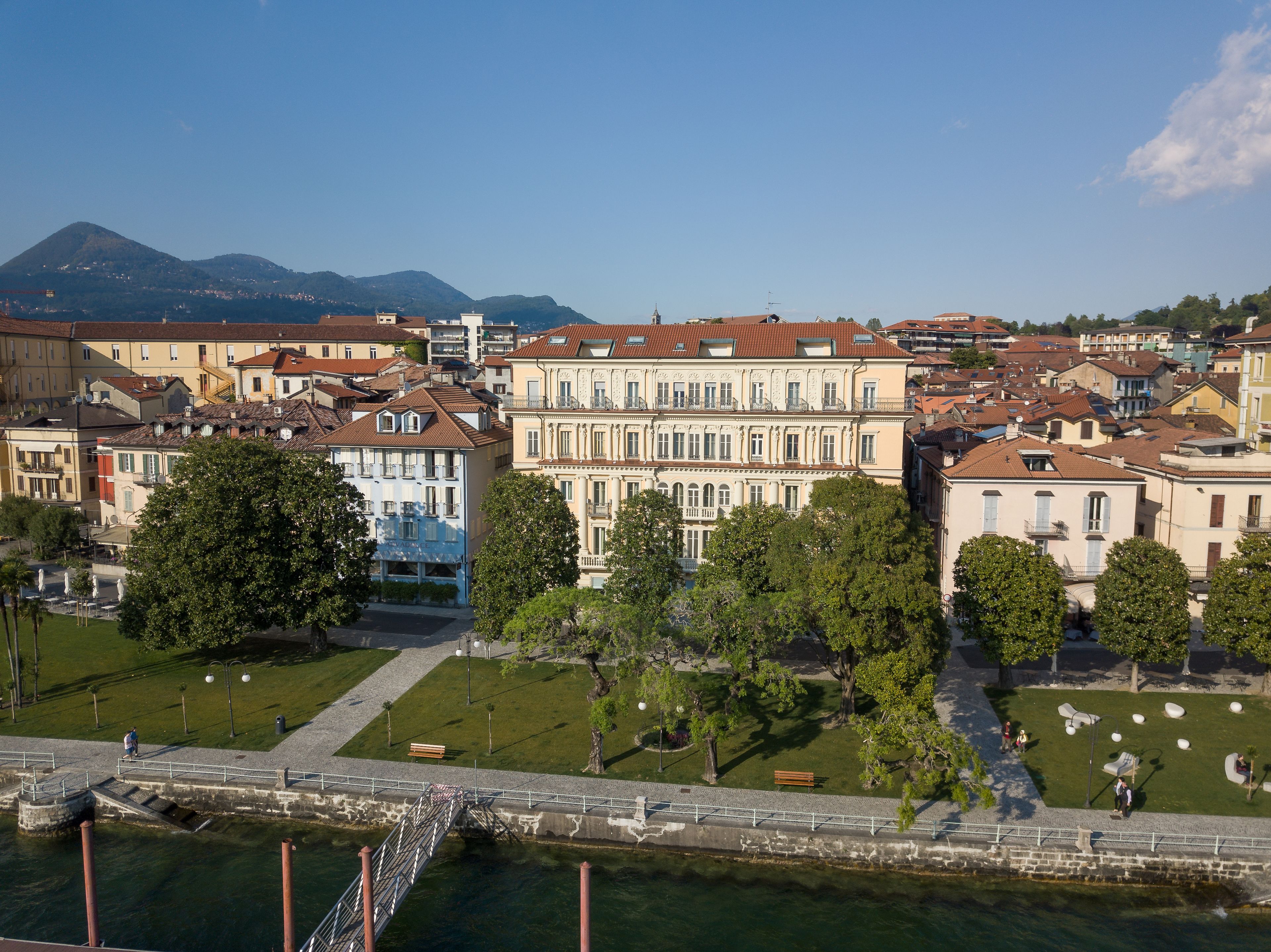 A riverside view of a historic town with buildings along the water, a bridge, and a park with benches.