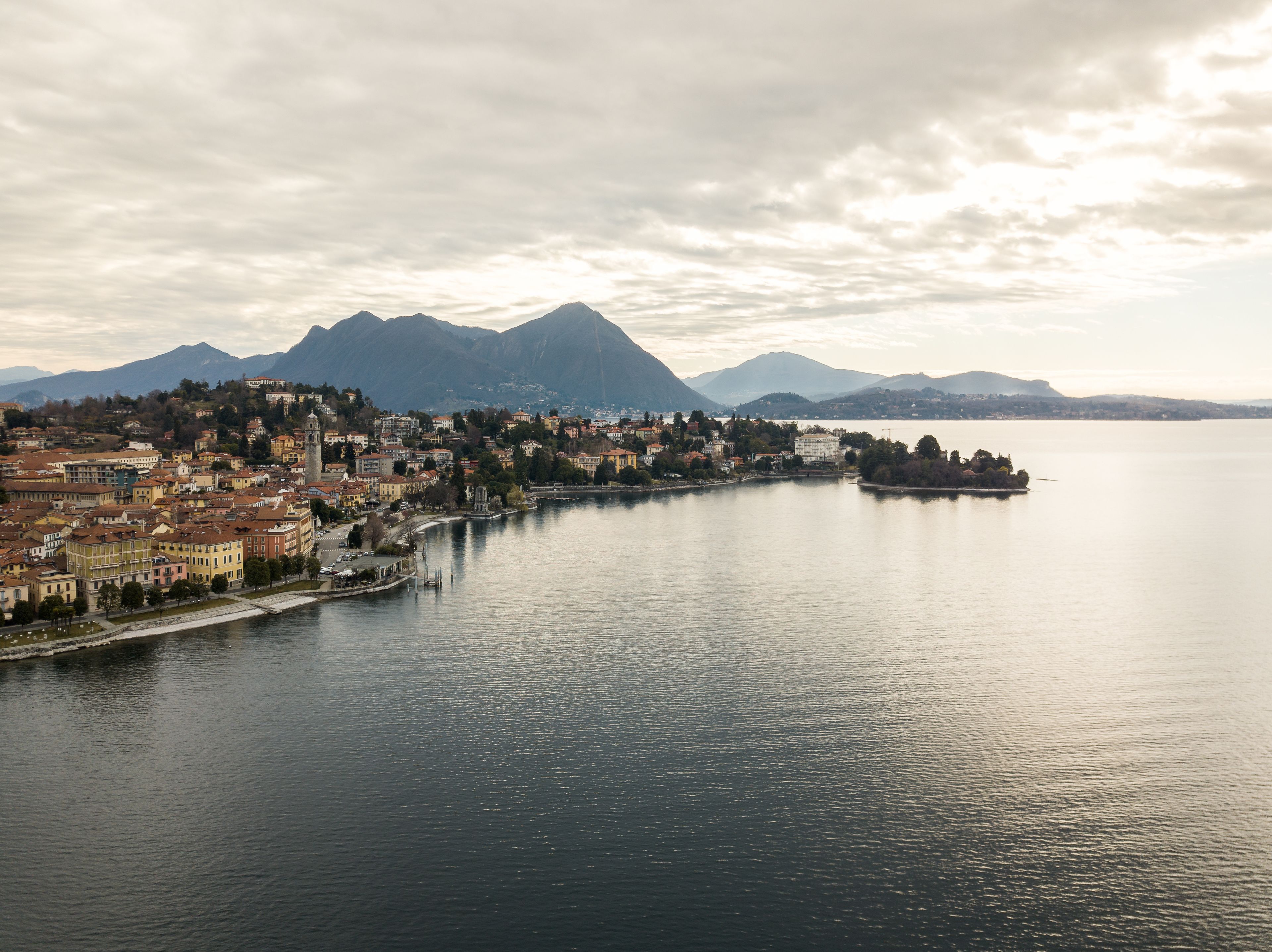 A panoramic view of a lakeside town with historic buildings, a prominent tower, and mountains in the background.