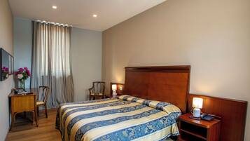 Une chambre d’hôtel avec un grand lit, un bureau avec une chaise, une table de chevet avec une lampe et un téléviseur fixé au mur.