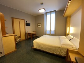 Una habitación de hotel con cama, escritorio, silla, armario y televisión.