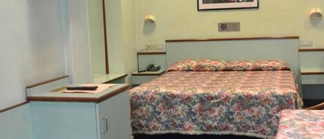 A bedroom with a bed, a desk, a chair, a mirror, and a wall-mounted TV.