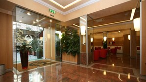 A modern lobby with a polished marble floor, glass doors leading to a reception area, and red seating in the background. - Le Petit Hotel (Turin)