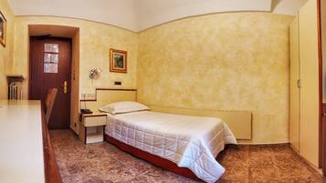 Um quarto pequeno e acolhedor com uma cama de casal, uma mesa de cabeceira, uma escrivaninha e uma cadeira.