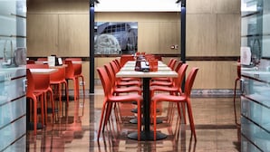 A modern dining area with a long table and red chairs, a glass partition on one side, and a view of a car through a window. - Le Petit Hotel (Turin)