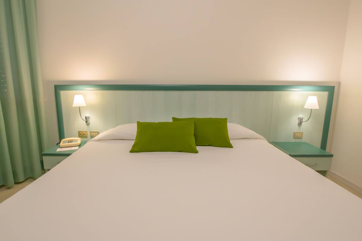 A neatly made bed with two pillows, two bedside tables with lamps, and a telephone on one of the tables.