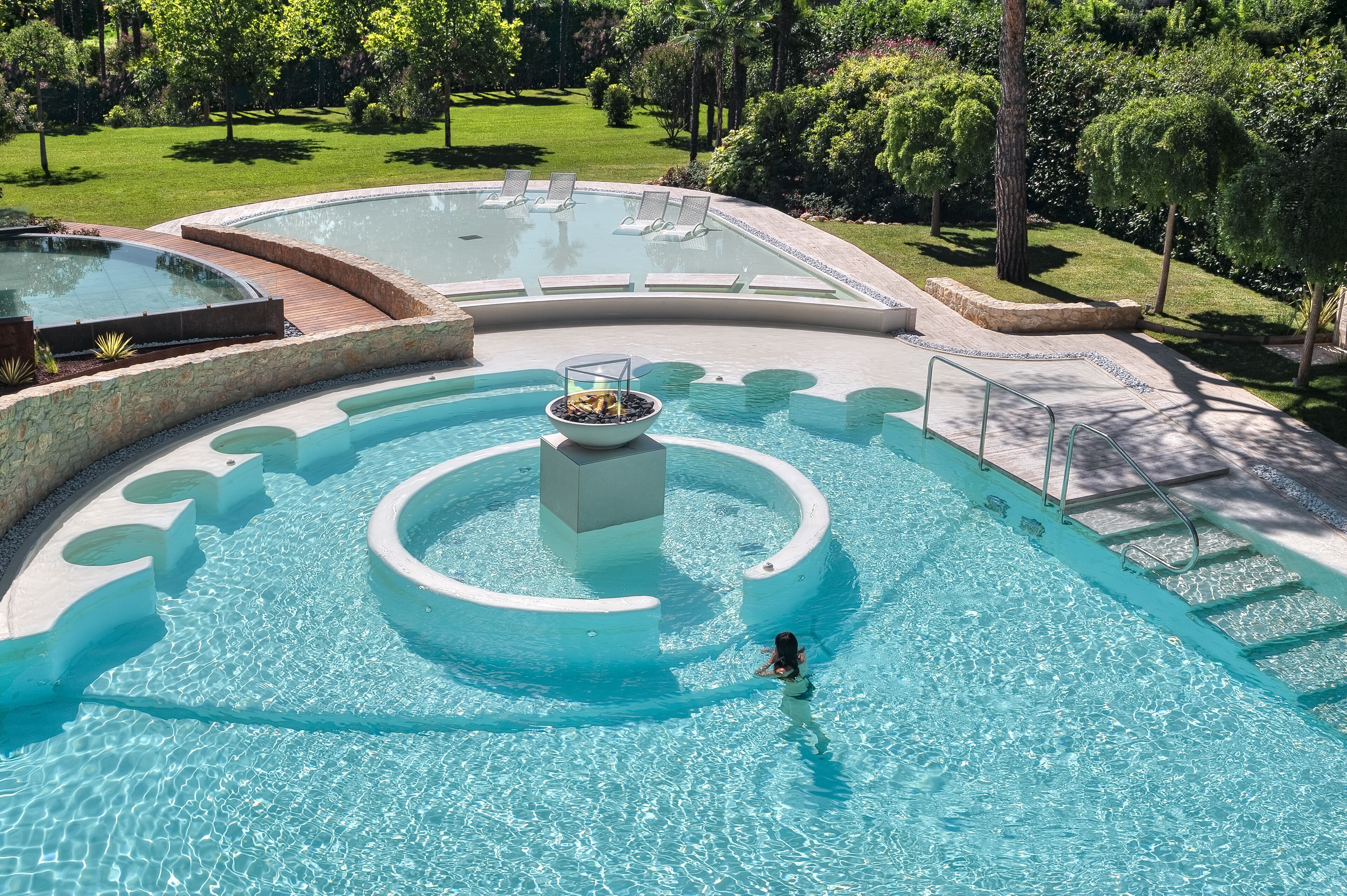 Ein großer, runder Pool mit einem zentralen Feuerbereich und mehreren Sitzbereichen darum herum.