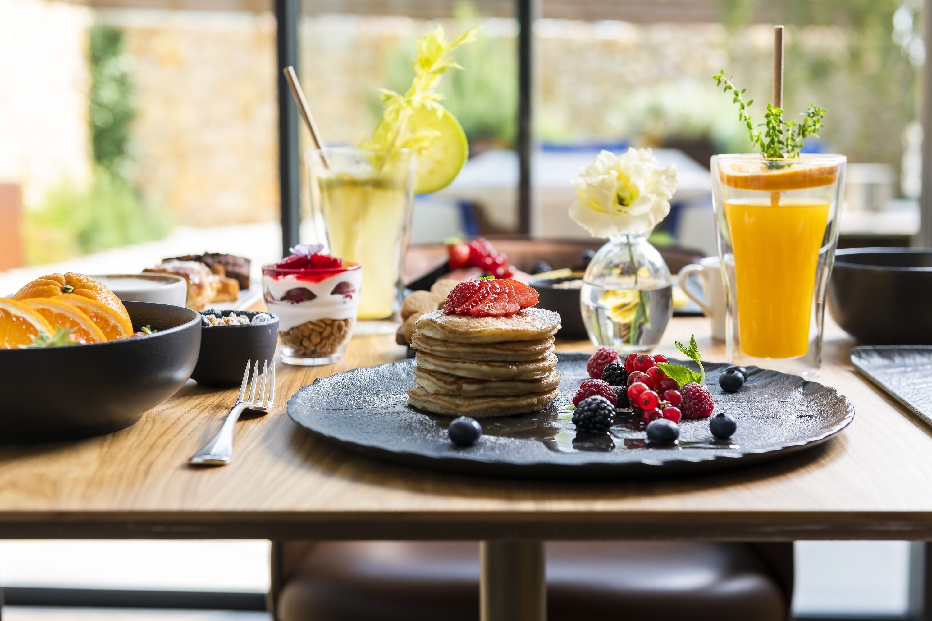 A breakfast setting with pancakes, berries, and a glass of orange juice on a wooden table.