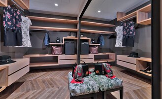 A modern room with wooden shelves displaying clothing and bags, a mirrored wall, and a bench with bags.