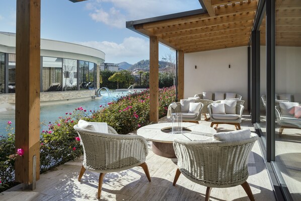 A covered outdoor seating area with wicker chairs and a fire pit, overlooking a swimming pool and mountains. - Esplanade Tergesteo - Luxury Retreat (Montegrotto Terme)