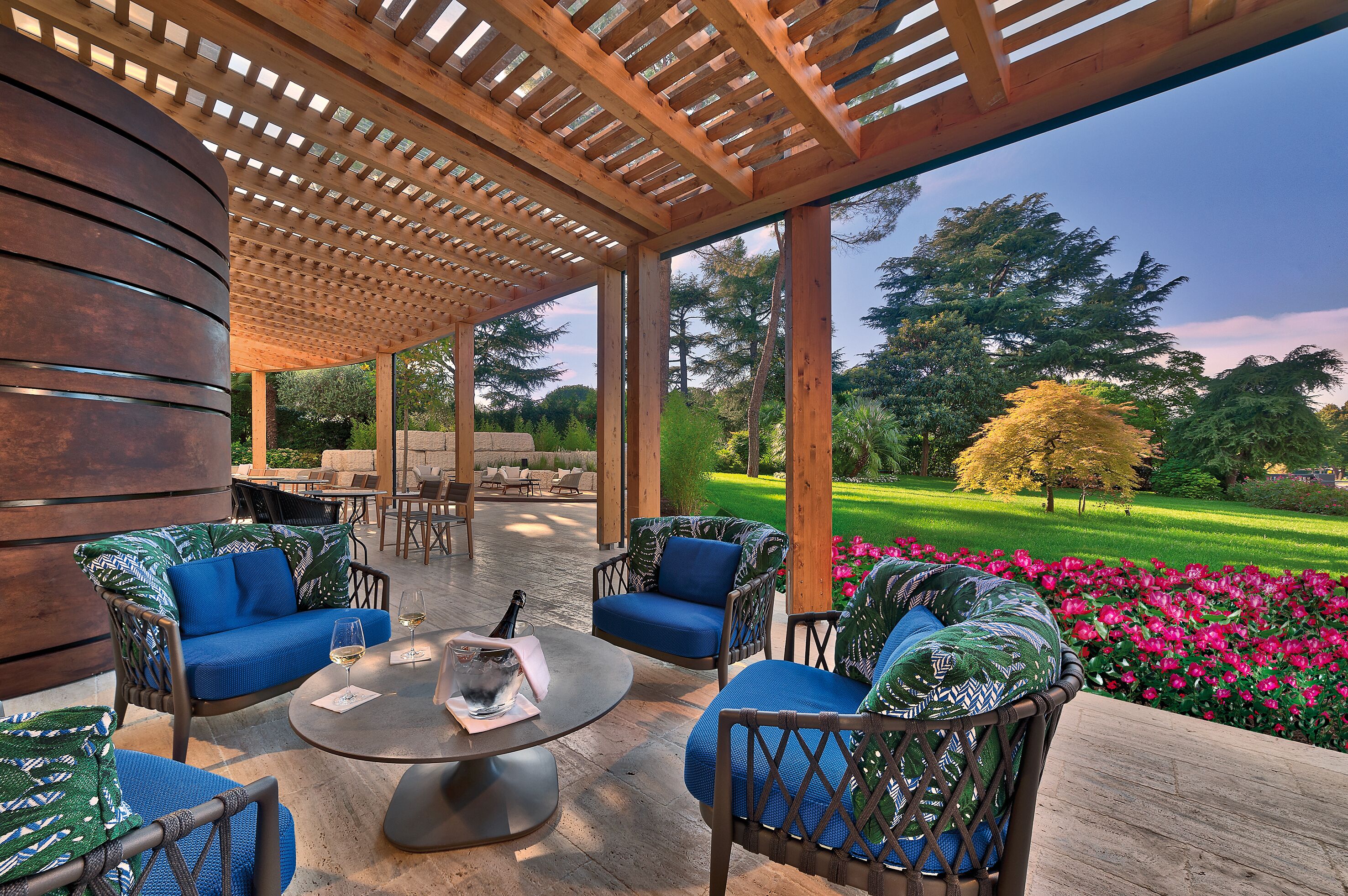 A covered outdoor seating area with wooden furniture and a view of a well-maintained garden.