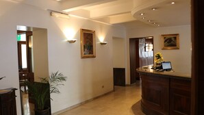 A hotel lobby with a reception desk, wall-mounted lighting, and a potted plant. - Hotel Italia (Turin)