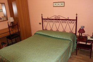 A bedroom with a green patterned bedspread, a wooden nightstand with a lamp, and a wall-mounted picture. - Hotel Italia (Turin)