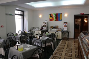 A dining area with tables and chairs, a buffet station, and a colorful abstract painting on the wall.