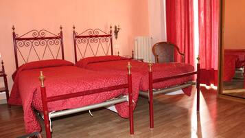 Ein Doppelbett mit Metallgestell und roter Bettwäsche, ein Holzstuhl und ein roter Vorhang.
