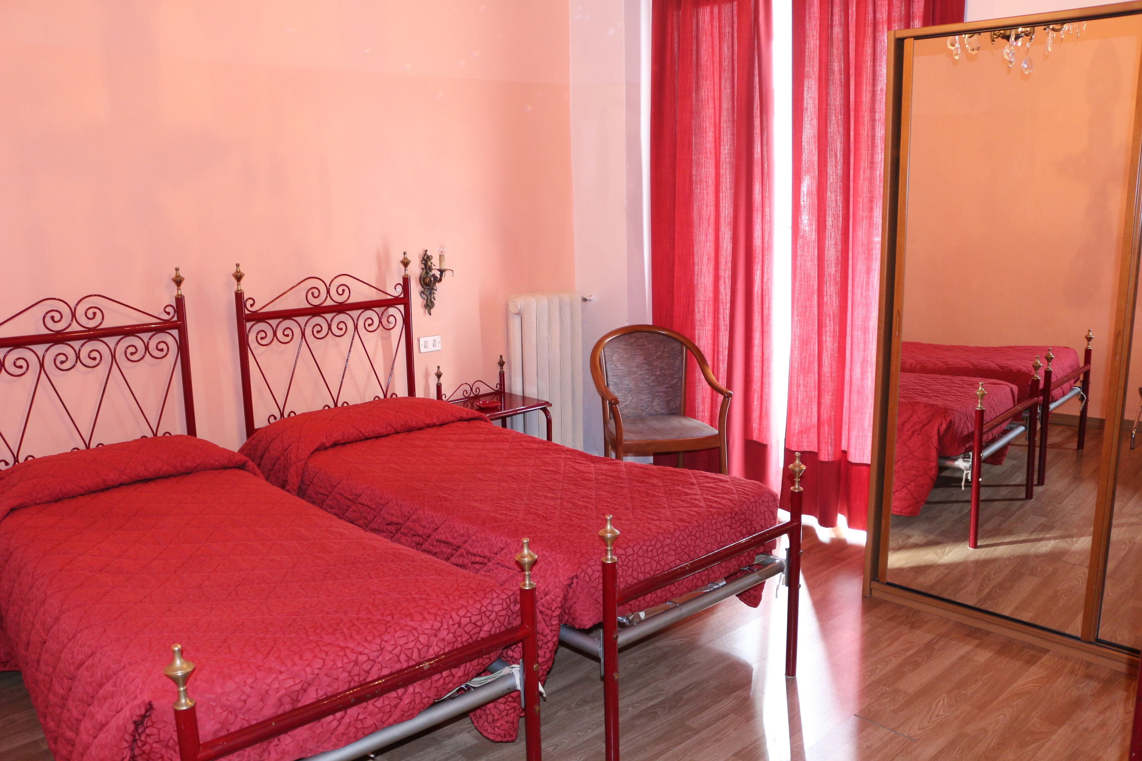 A bedroom with two beds, a chair, a mirror, and a radiator.