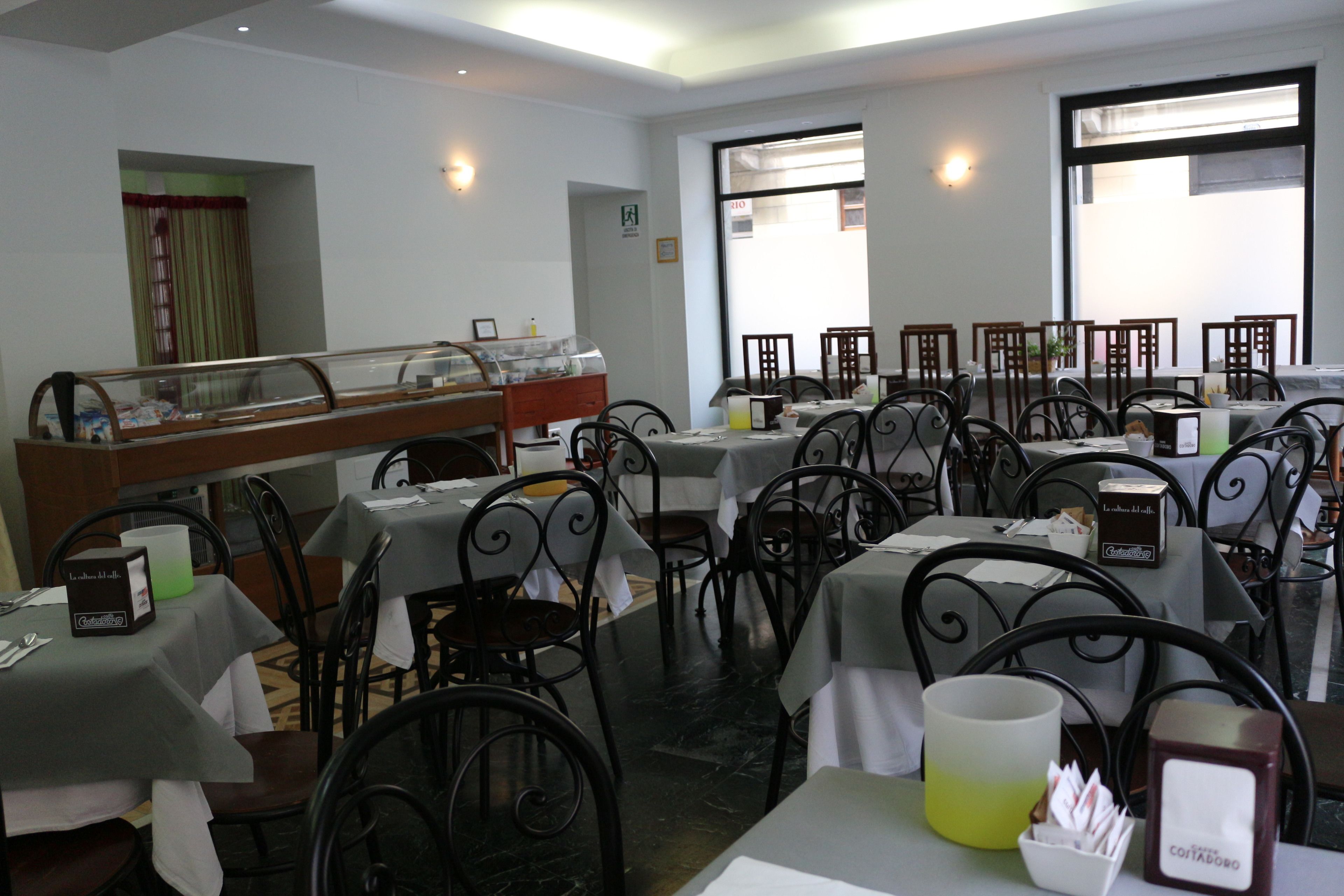 A restaurant with multiple tables and chairs, a buffet area, and a view of the street through large windows.