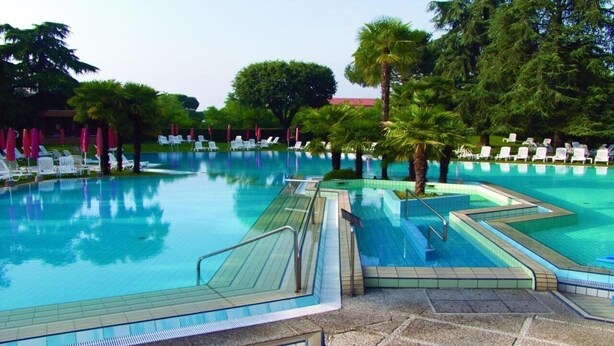 Ein Schwimmbecken mit mehreren Bahnen, umgeben von Palmen und Liegestühlen.