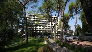 Ein mehrstöckiges Hotel mit einem steinbelagten Weg, der zum Eingang führt, umgeben von Grünflächen und Bäumen.