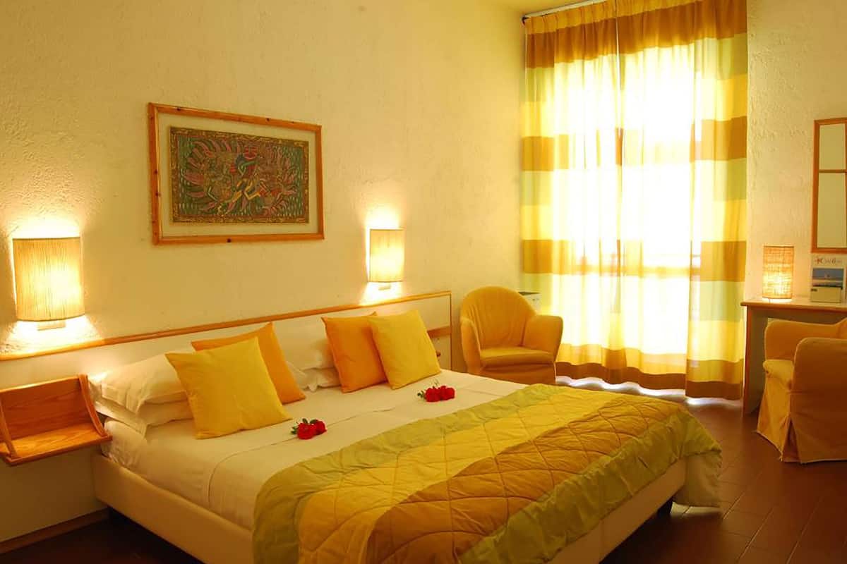 A hotel room with a bed, two bedside lamps, a chair, a desk, and a window with curtains.