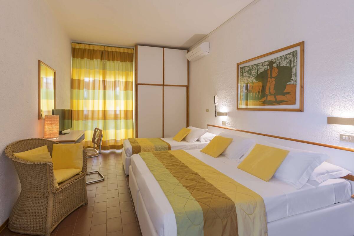 A hotel room with two beds, a chair, a desk, and a large window with curtains.