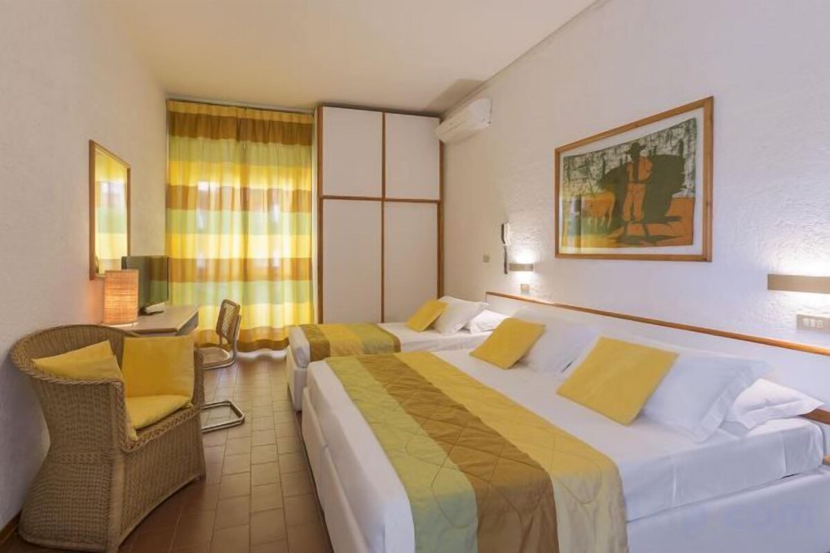 A hotel room with two beds, a chair, a desk, and a painting on the wall.