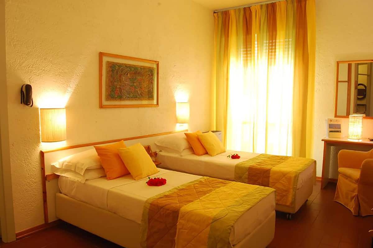 A hotel room with two beds, a desk, a chair, a painting on the wall, and a window with curtains.