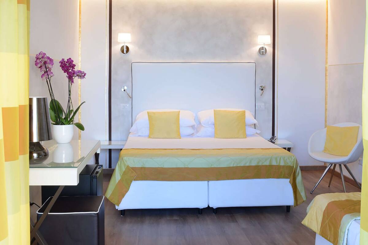 A hotel room with a bed, bedside tables, a chair, and a potted plant.