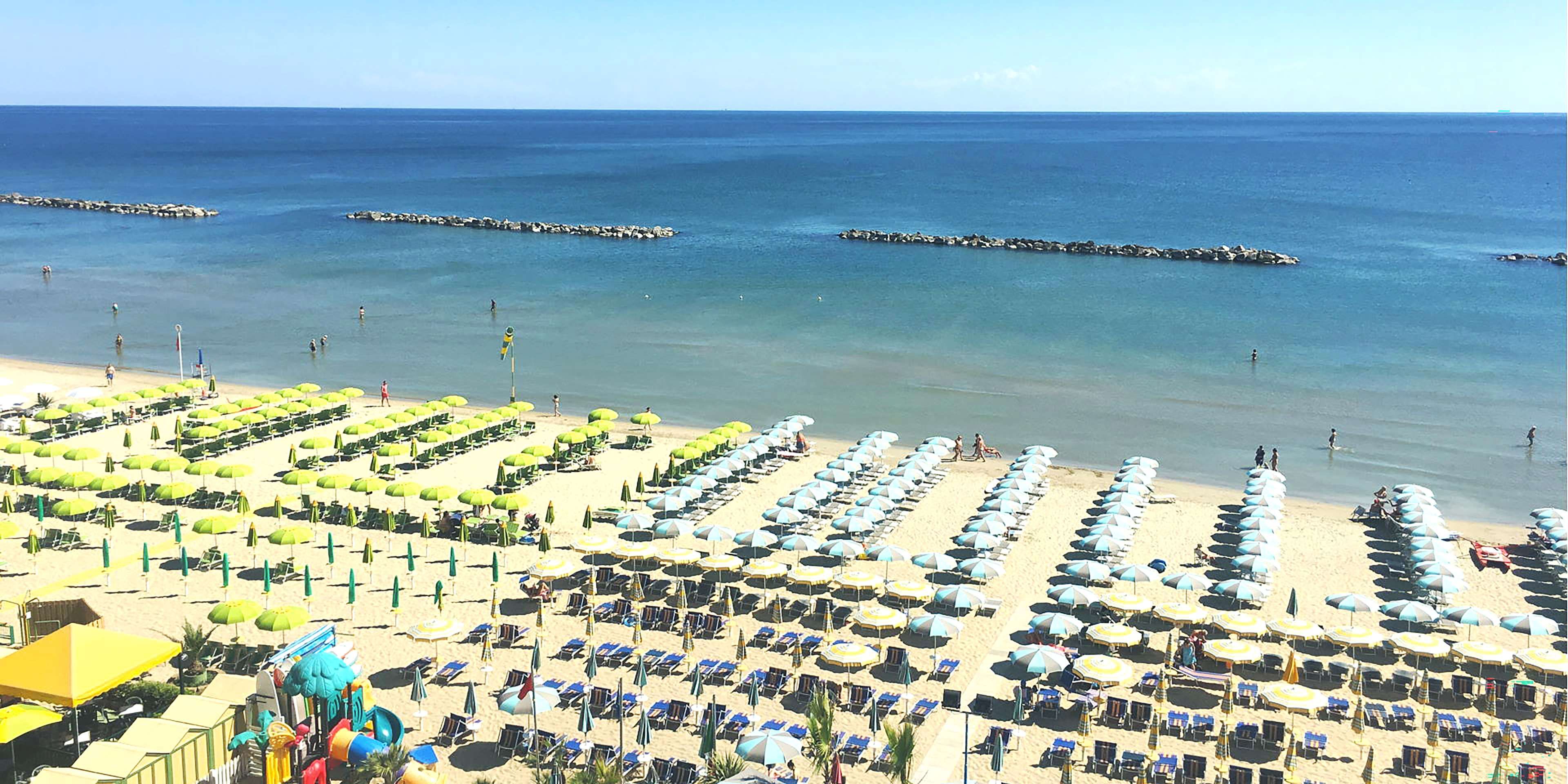 A beach with rows of sunbeds and umbrellas, a clear sky, and calm sea.