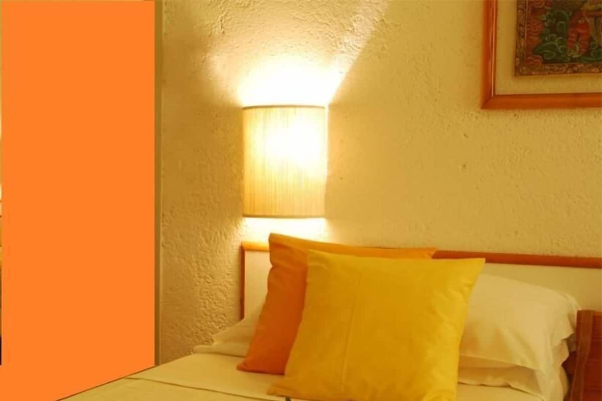 A bed with yellow and white bedding, a red rose on the bed, and a wall-mounted lamp.