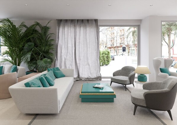 A modern living room with a white sofa, teal cushions, a grey armchair, and a coffee table with books. There are potted plants and a view of the street through large windows. - Hotel Bellevue (Pesaro)
