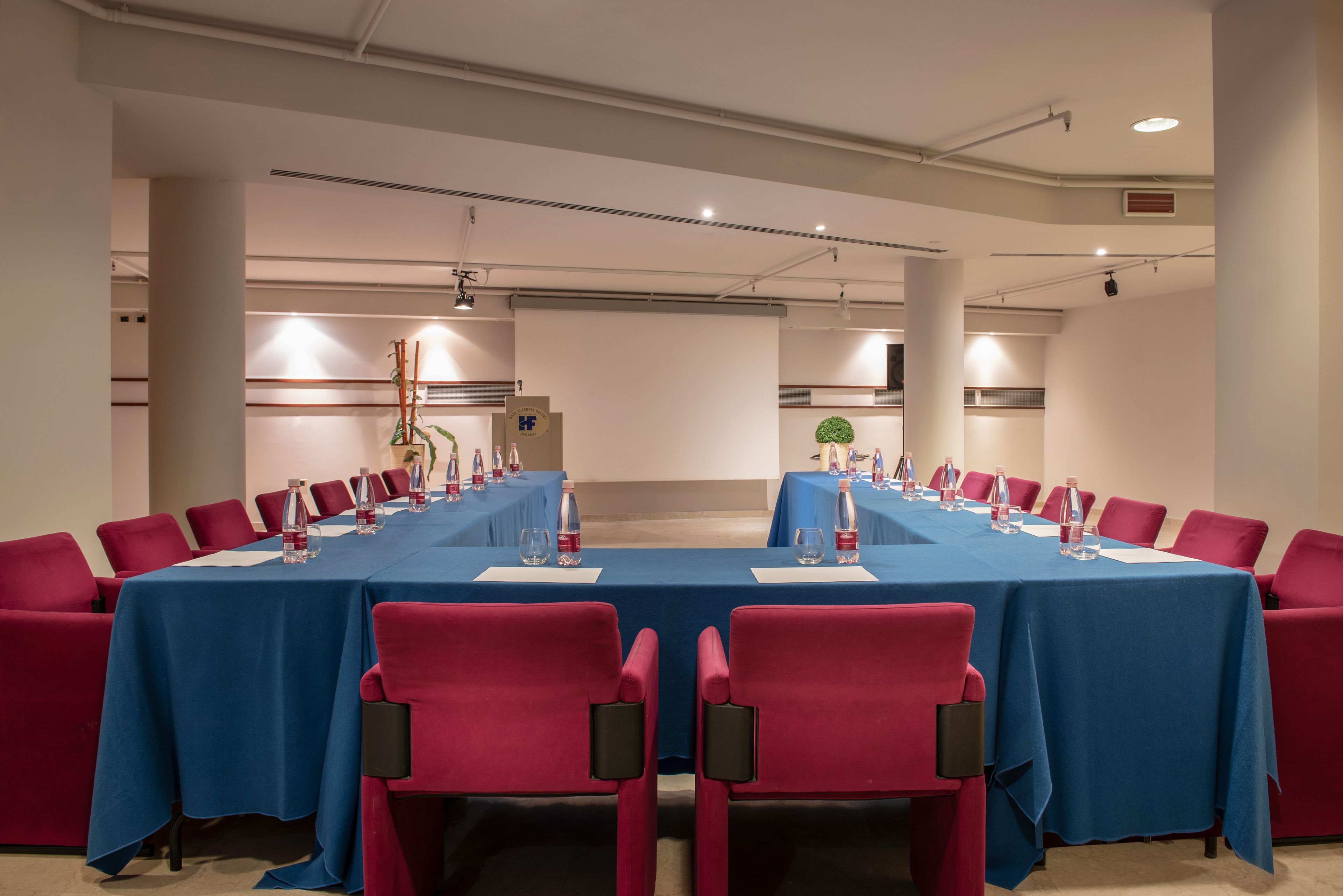 A conference room with a long table, red chairs, and water bottles.