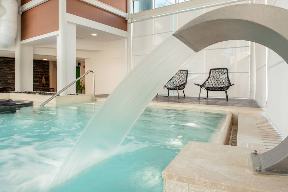 Una piscina con tobogán de agua, dos sillas y un muro de piedra.
