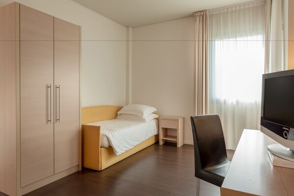 A modern hotel room with a bed, a desk, a TV, and a wardrobe.