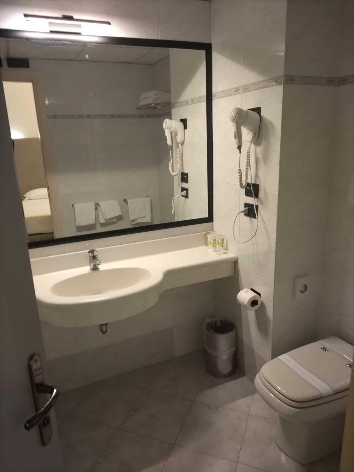 A bathroom with a sink, mirror, hairdryer, and toilet.