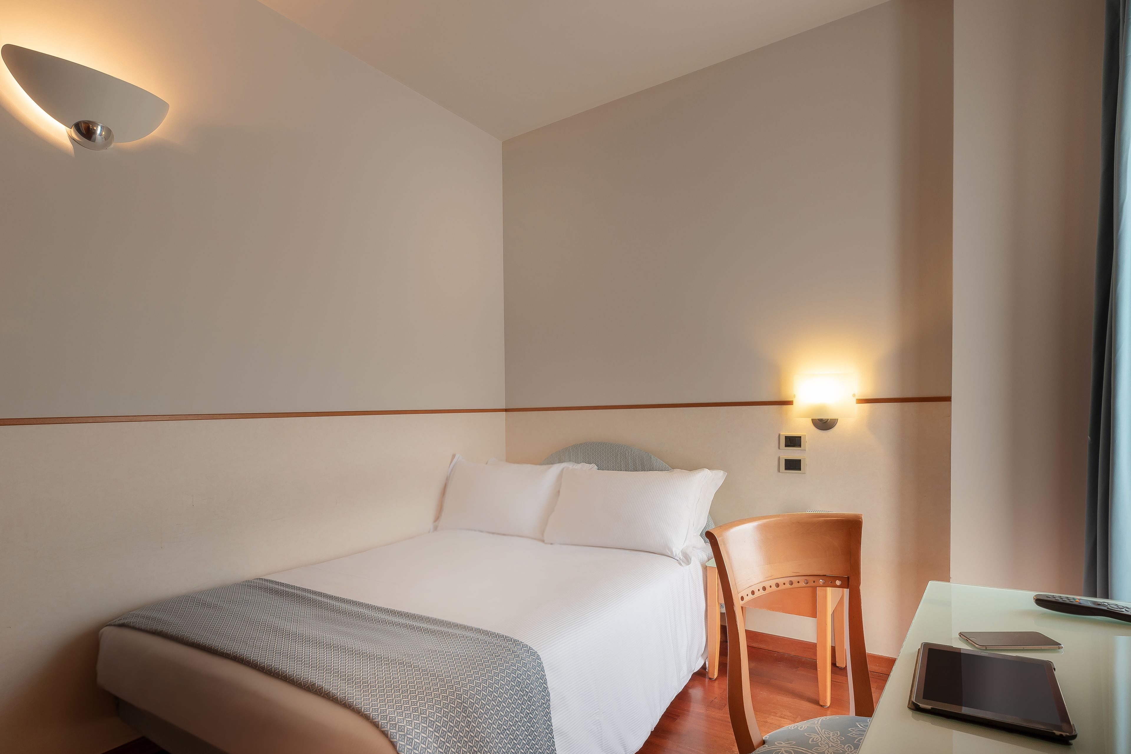A hotel room with a bed, a desk, a chair, and a nightstand.