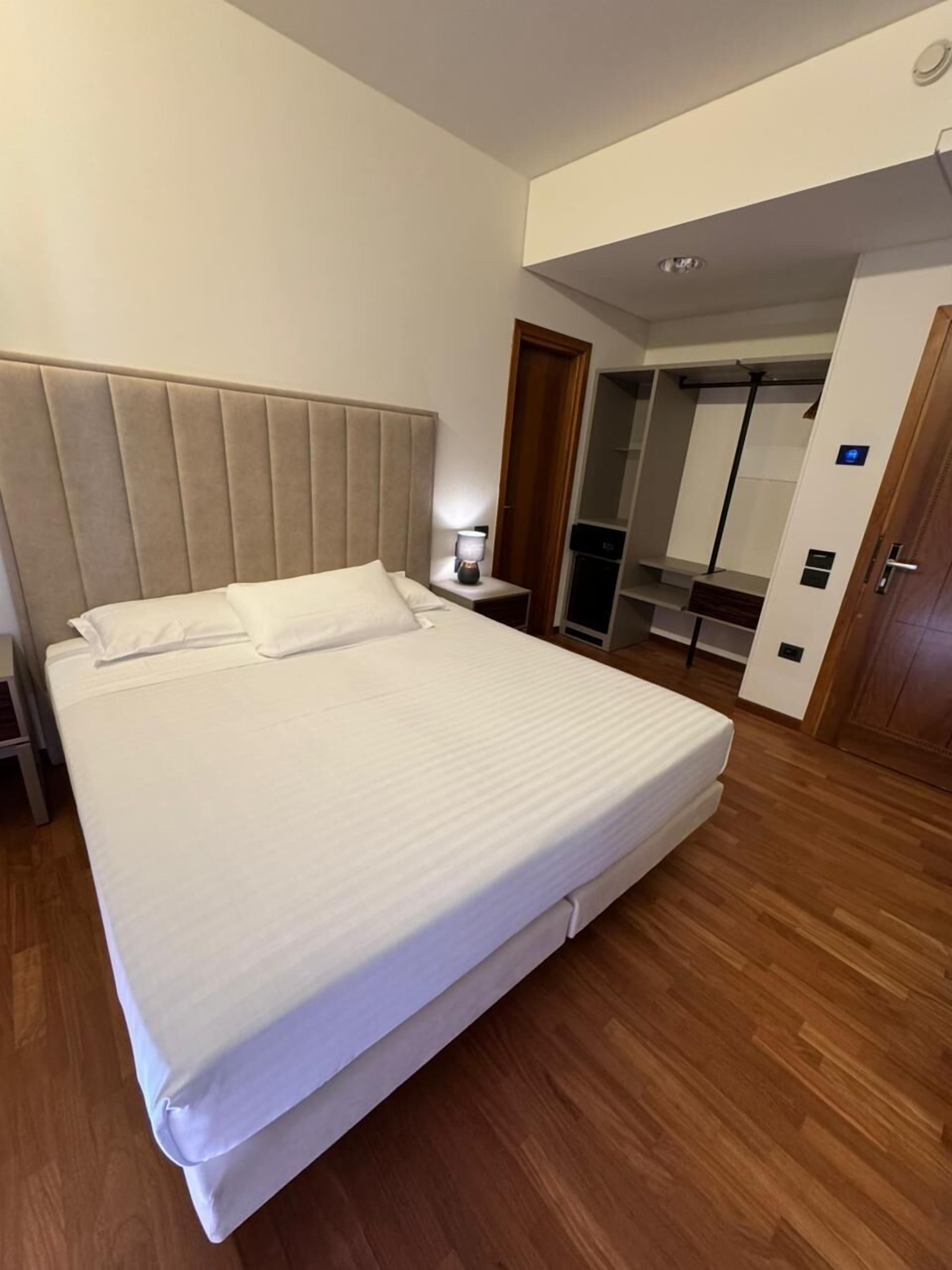 A hotel room with a large bed, a bedside table with a lamp, a wardrobe, and a mirror.