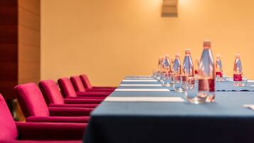 Ein Konferenzraum mit Reihen roter Stühle und einem langen Tisch, auf dem Wasserflaschen und Gläser stehen.