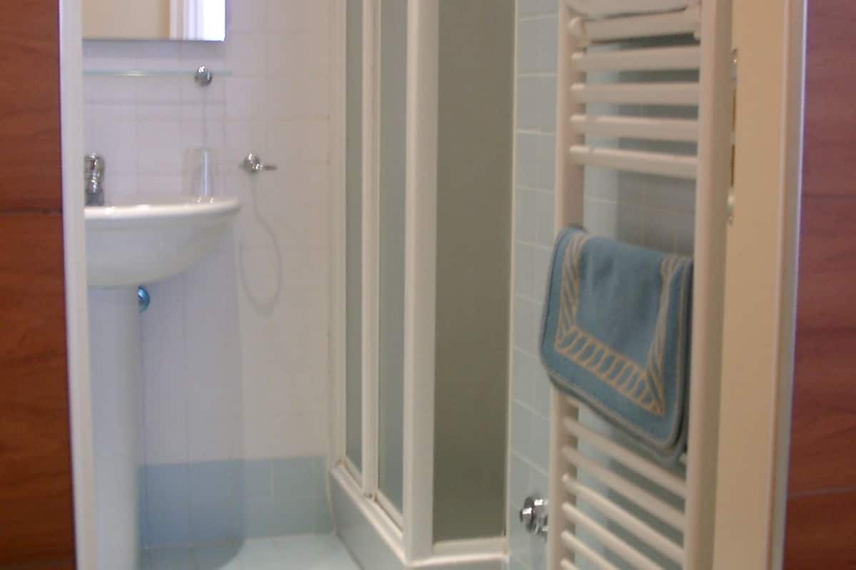 A bathroom with a sink, mirror, shower, and towel rack.