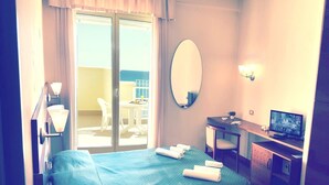 A hotel room with a bed, a desk with a TV, a chair, a mirror, and a view of the outdoors through a sliding door. - Gala (Pesaro)