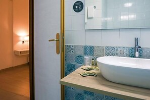 A bathroom with a large white sink, patterned tiles, a towel dispenser, and a door with a brass handle. - Hotel Arcadia (Macerata)