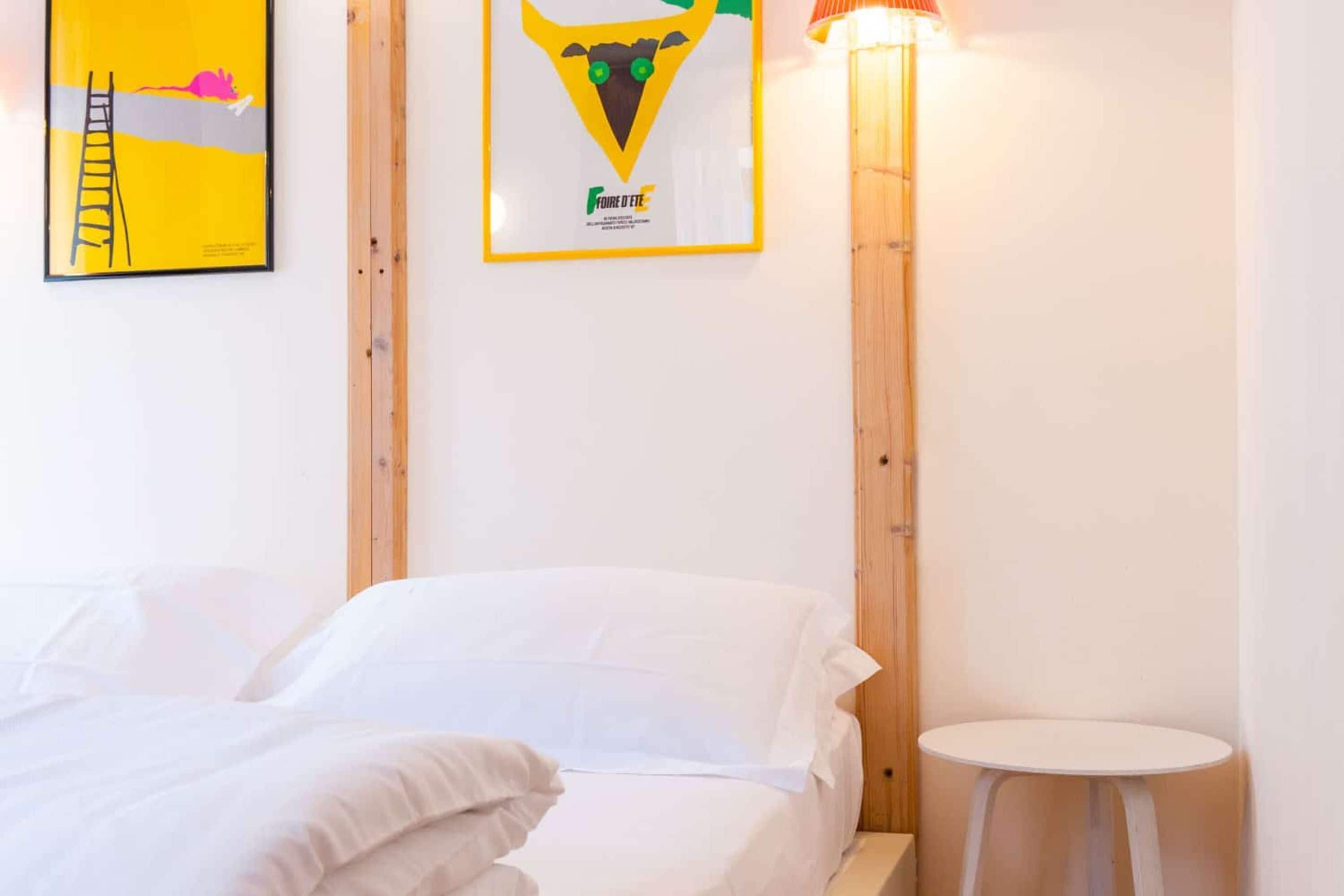A hotel room with a bed, a small round table, and two wall-mounted artworks.