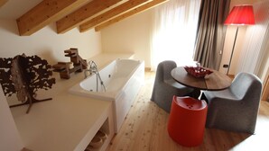 A modern bathroom with a bathtub, wooden beams, a red stool, and a table with a lamp.
