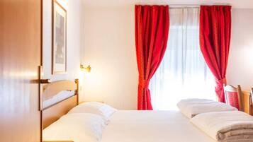 A hotel room with a bed, a nightstand, a framed picture on the wall, and red curtains.