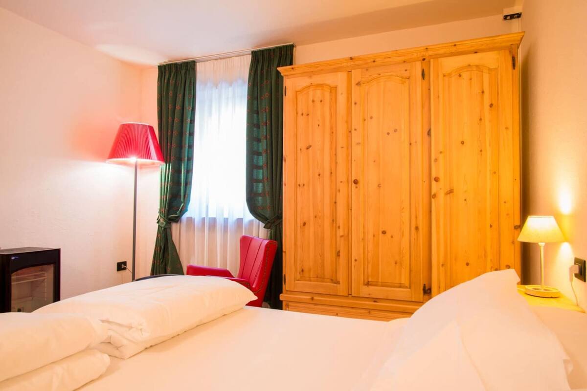 A hotel room with two beds, a wardrobe, a red chair, and a floor lamp.