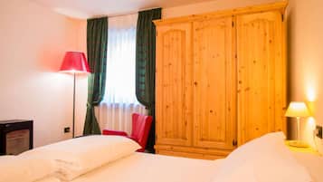 A hotel room with two beds, a wardrobe, a red chair, and a floor lamp.